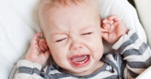 An image of a baby crying and pulling at their ears.